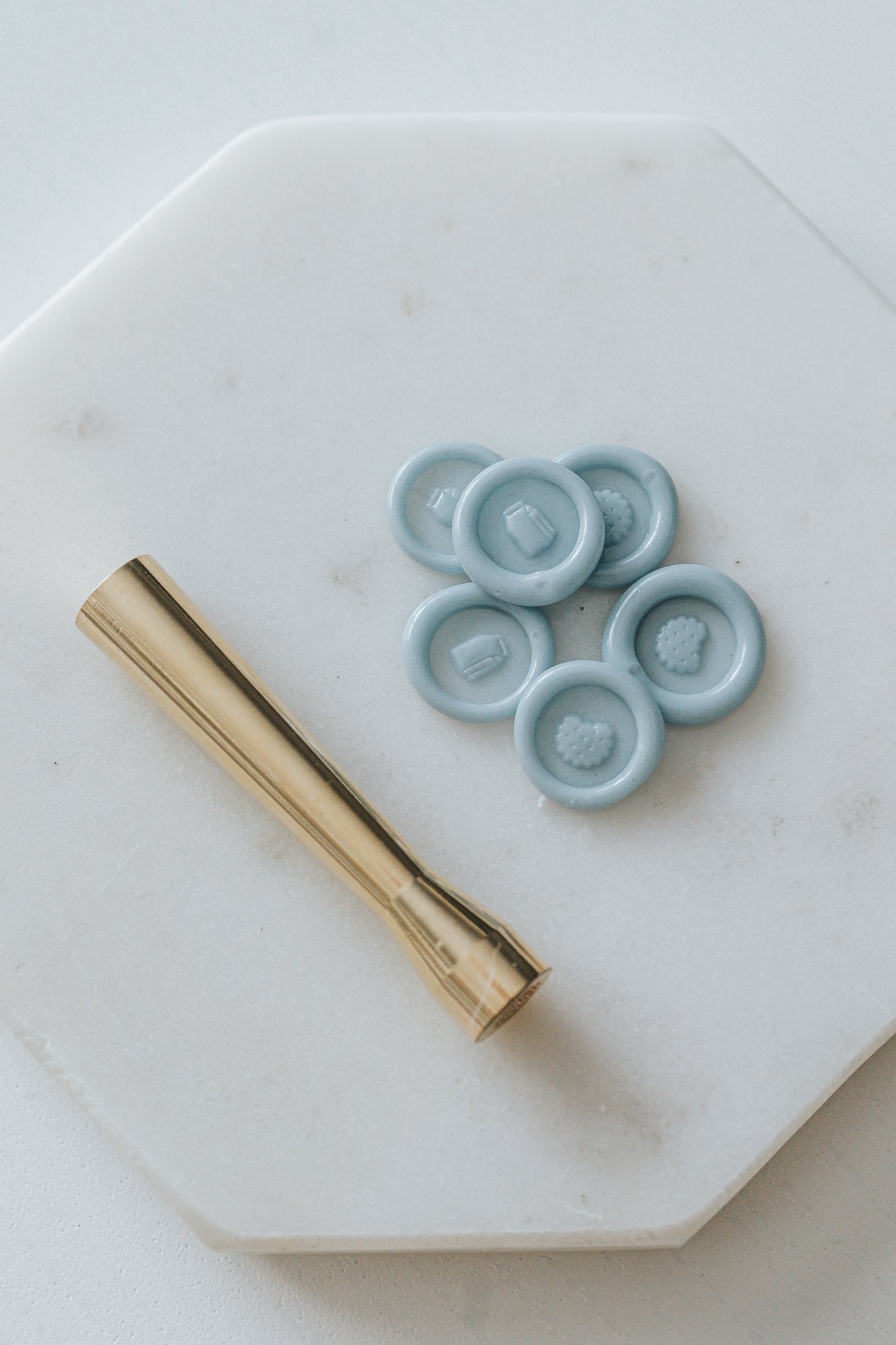 Gold miniature wax seal stamp with cookie and milk designs, placed on a white marble surface with matching blue wax seal