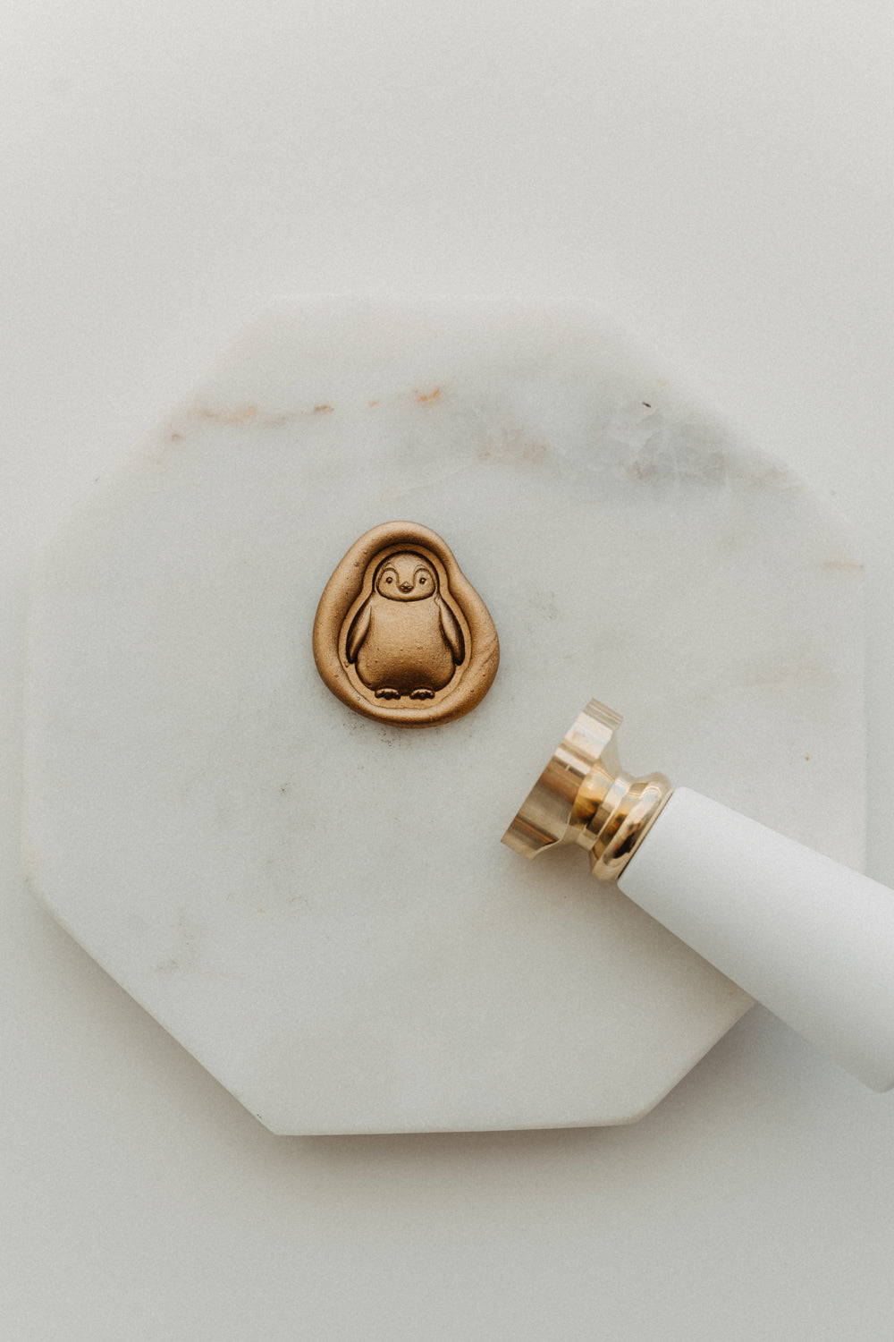 Gold penguin wax seal and white-handled brass wax seal stamp on a white marble tile.