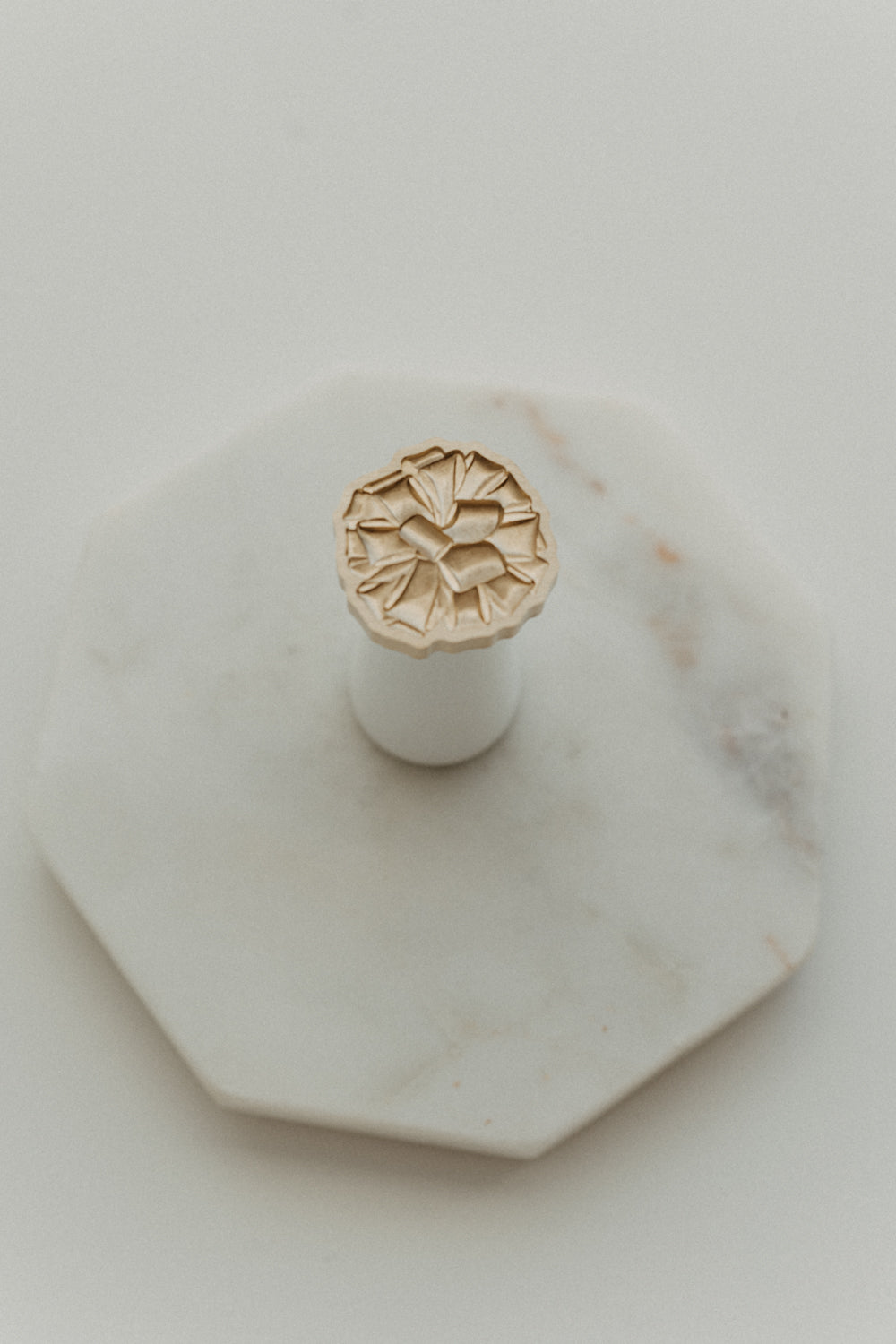 Gift bow wax seal stamp with brass design and white wooden handle on octagonal marble tray