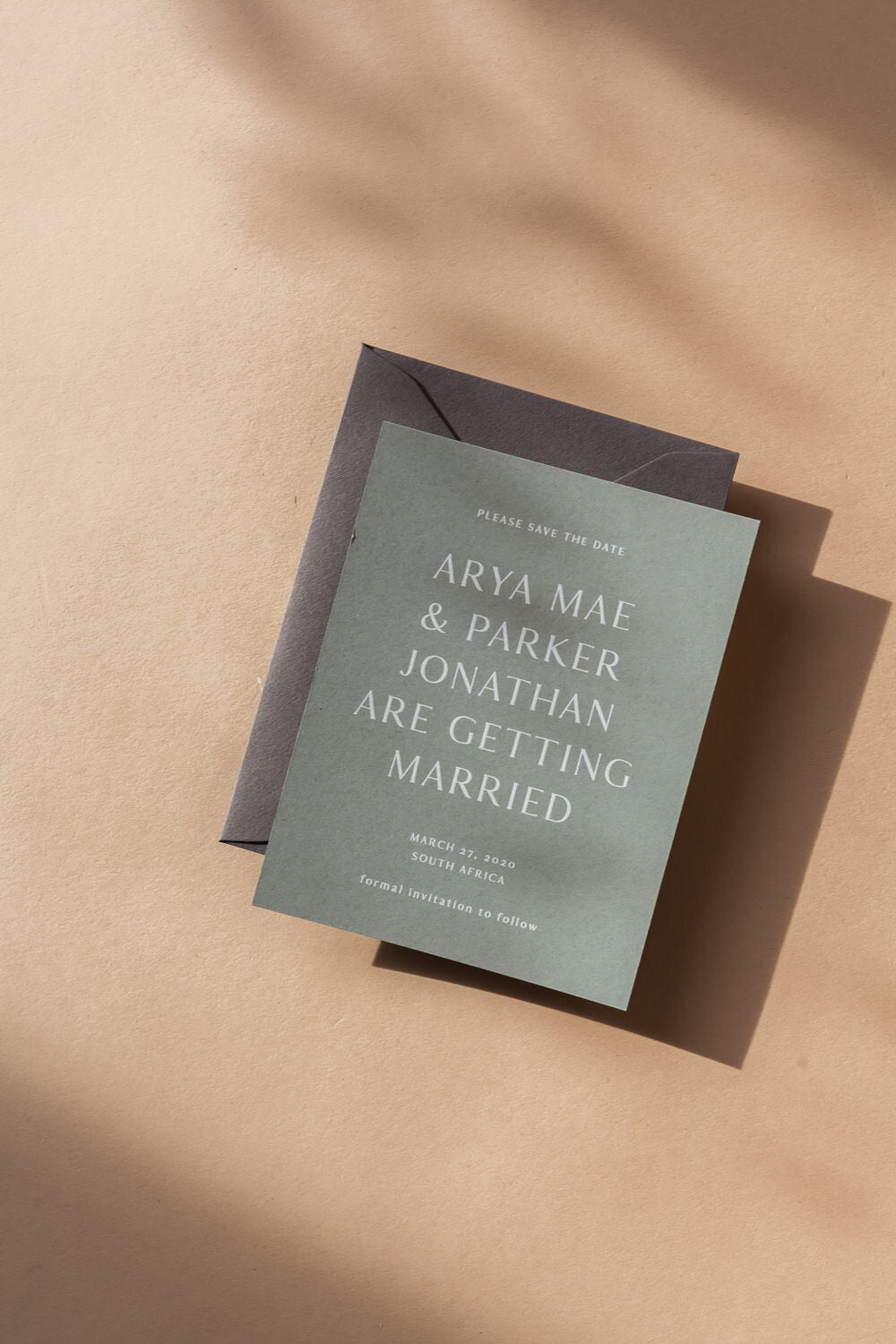 Minimalist save the date card with modern calligraphy text, green wedding stationery and envelope on neutral background
