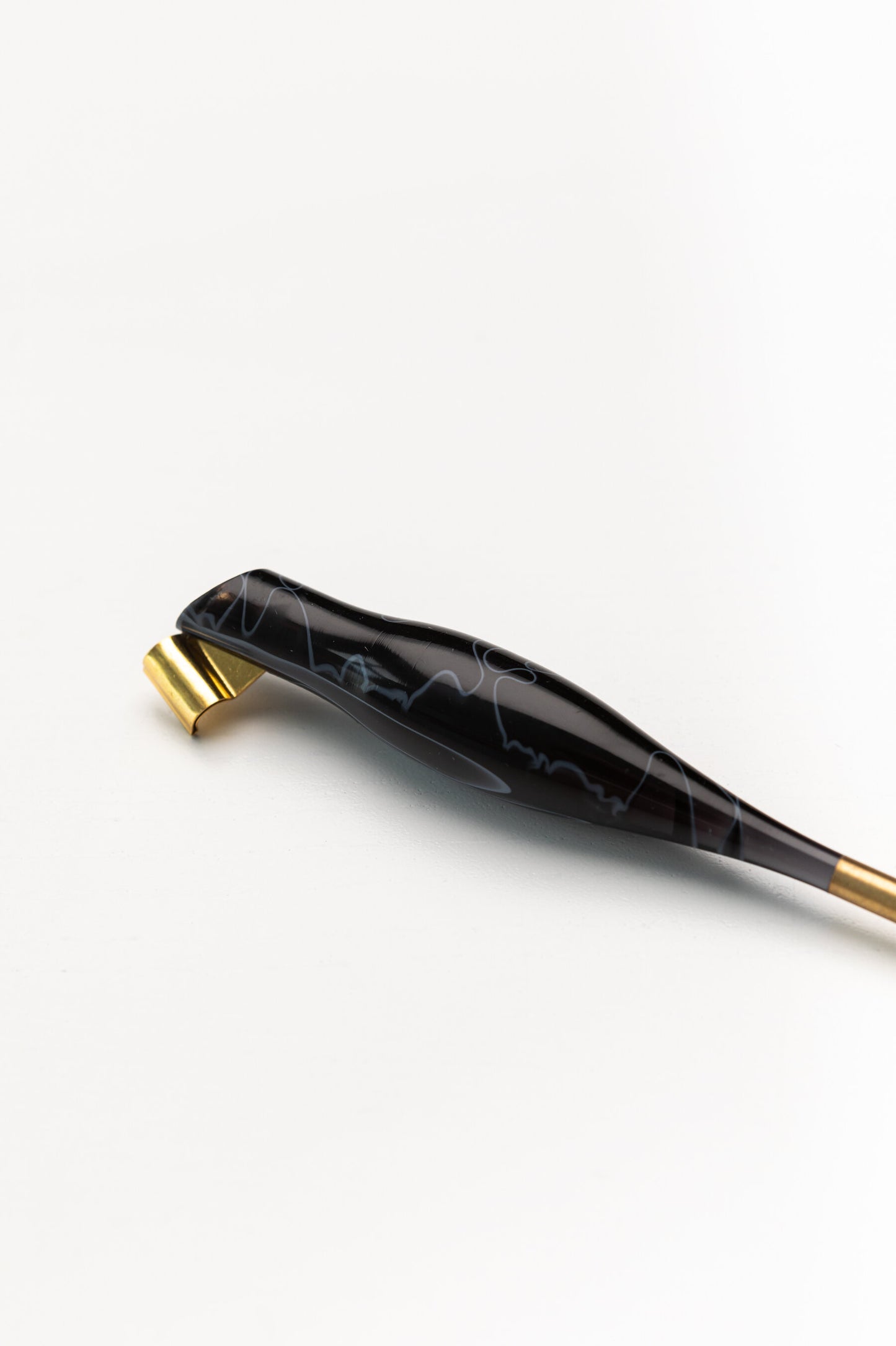 Close-up of a sleek black oblique calligraphy pen with white marbled patterns and a gold brass flange, on a white background