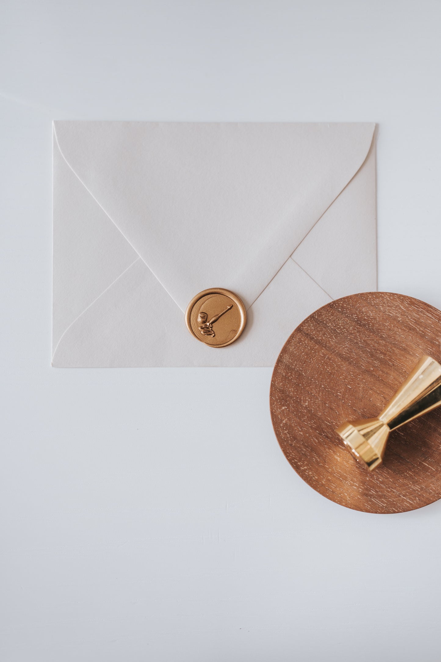 A brass wax seal stamp and beige envelope featuring a golden wax seal with a calligraphy penholder and ink jar design