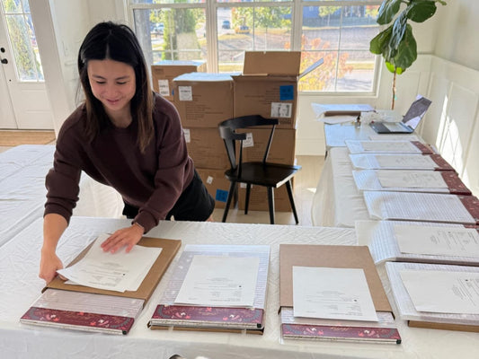 Karla preparing Brush Calligraphy Advent Calendars for shipment, organizing and labeling packages on a long table filled with boxed calendars