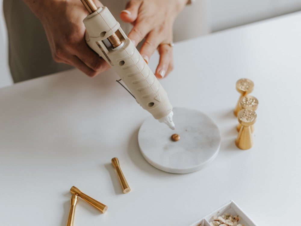 Close-up of a dual temperature glue gun creating a mini wax seal on a marble mat with brass mini wax seal stamps, demonstrating modern wax sealing tools for stationery, invitations, and handmade cards.