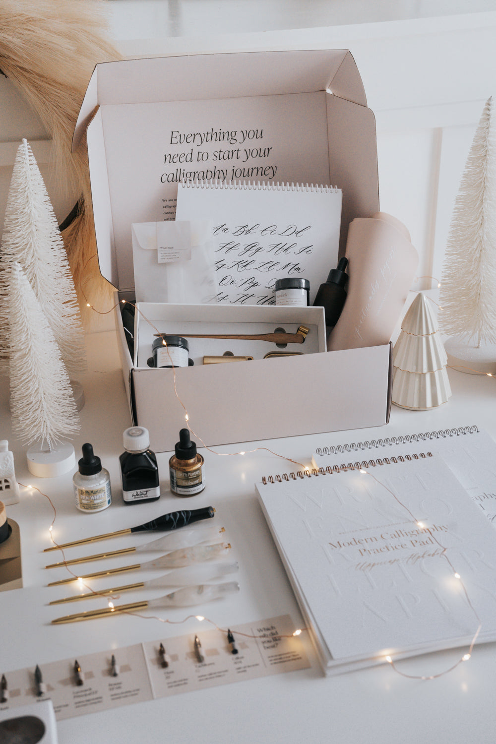 Beginner Calligraphy Starter Kit surrounded by ink samplers, penholders, nib samplers, practice pads, and fairy lights.