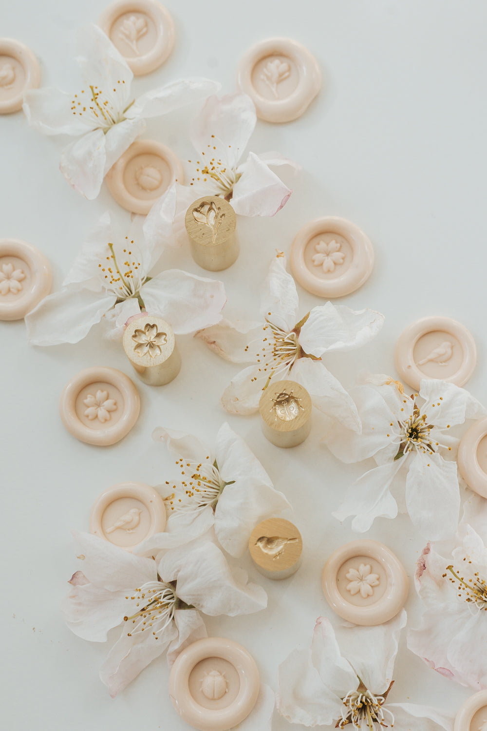 Two double-sided brass mini wax seal stamp on a white marble coaster and four gold mini wax seals