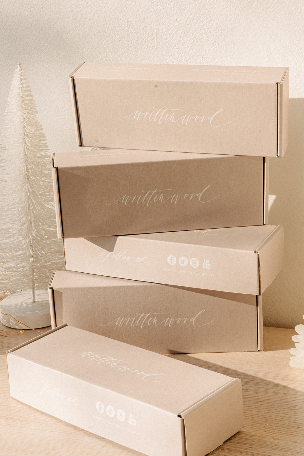 Stack of Written Word branded boxes on wooden table in golden hour light, representing calligraphy and wax seal bundles.