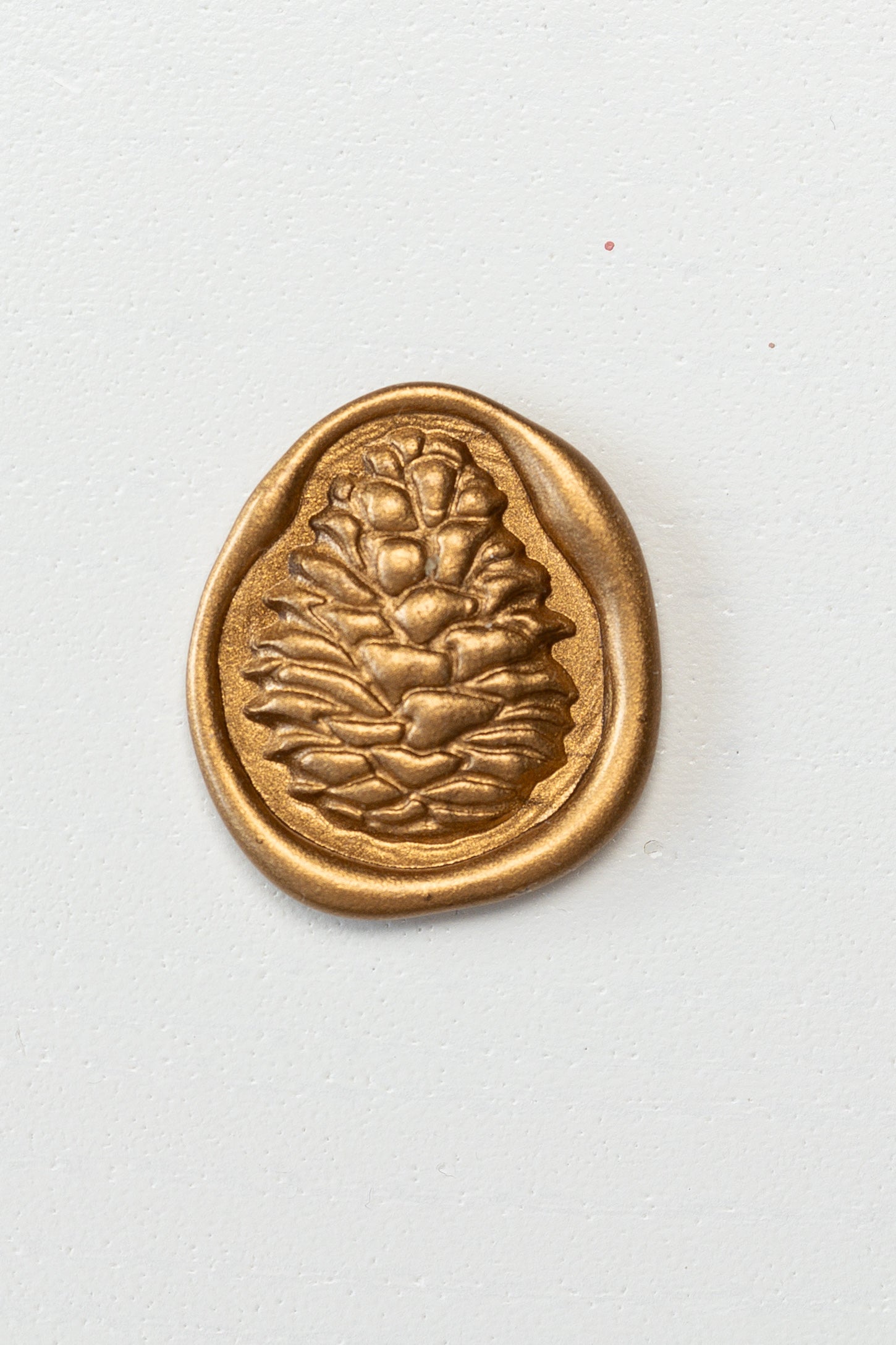 A golden 3D pinecone wax seal on a white surface