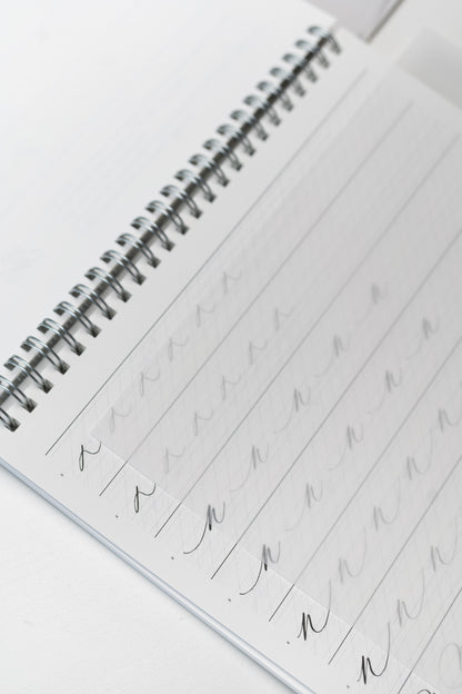 Spiral-bound calligraphy workbook with practice sheets and vellum overlays for tracing and improving letterforms