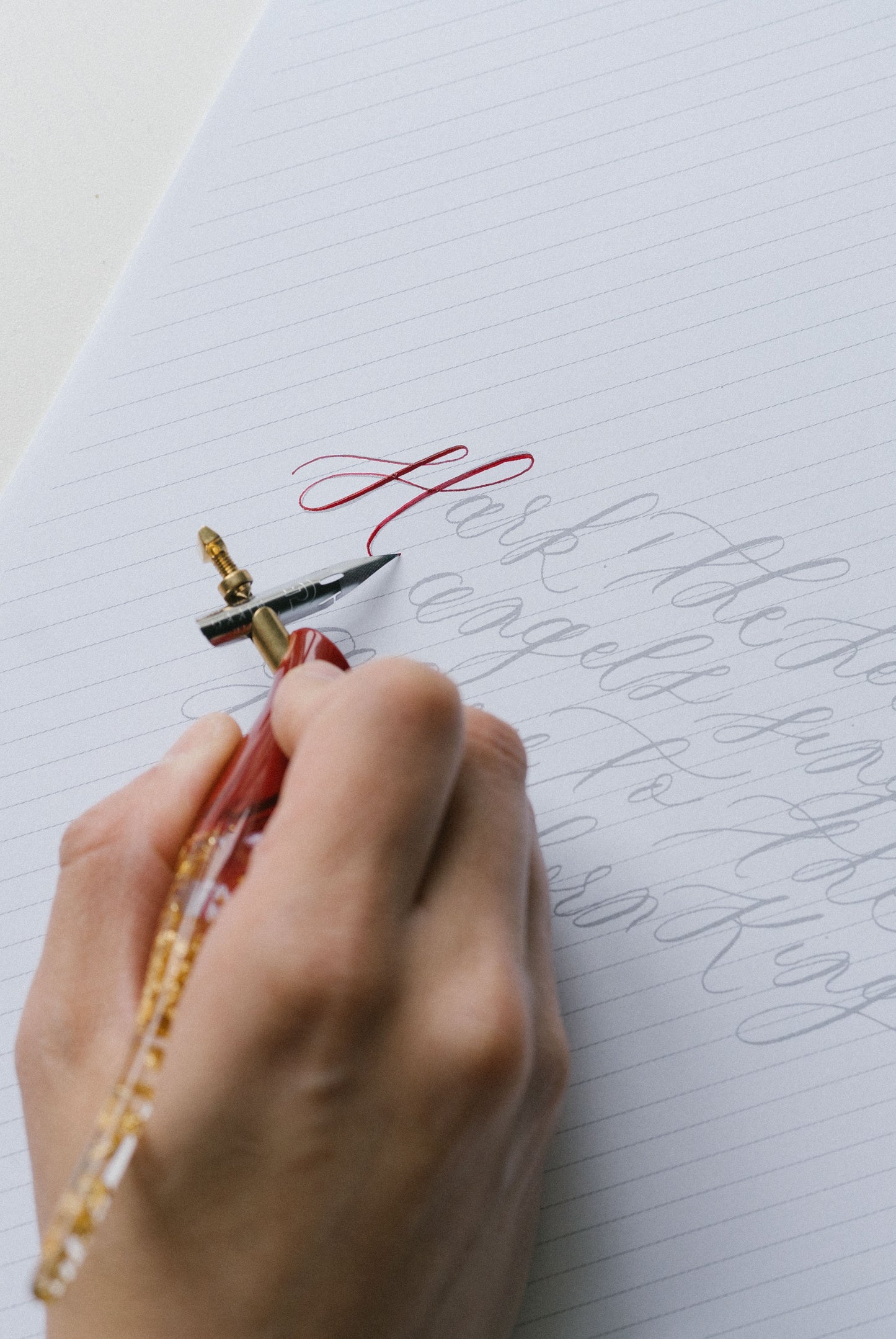 Close-up of oblique calligraphy pen tracing with red ink flourishes on calligraphy practice sheet