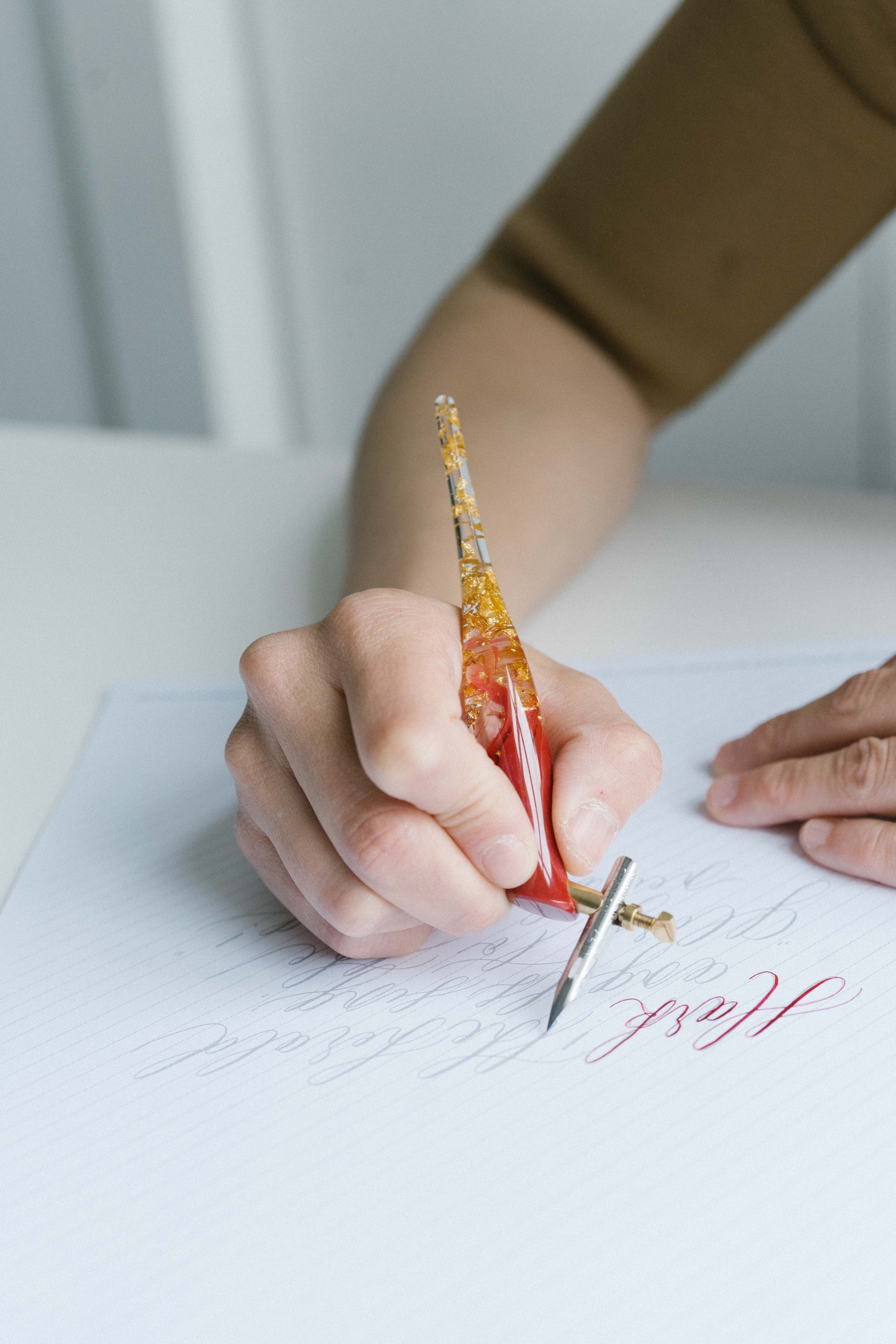 Hand using oblique calligraphy pen with red and gold holder tracing script on lined practice paper