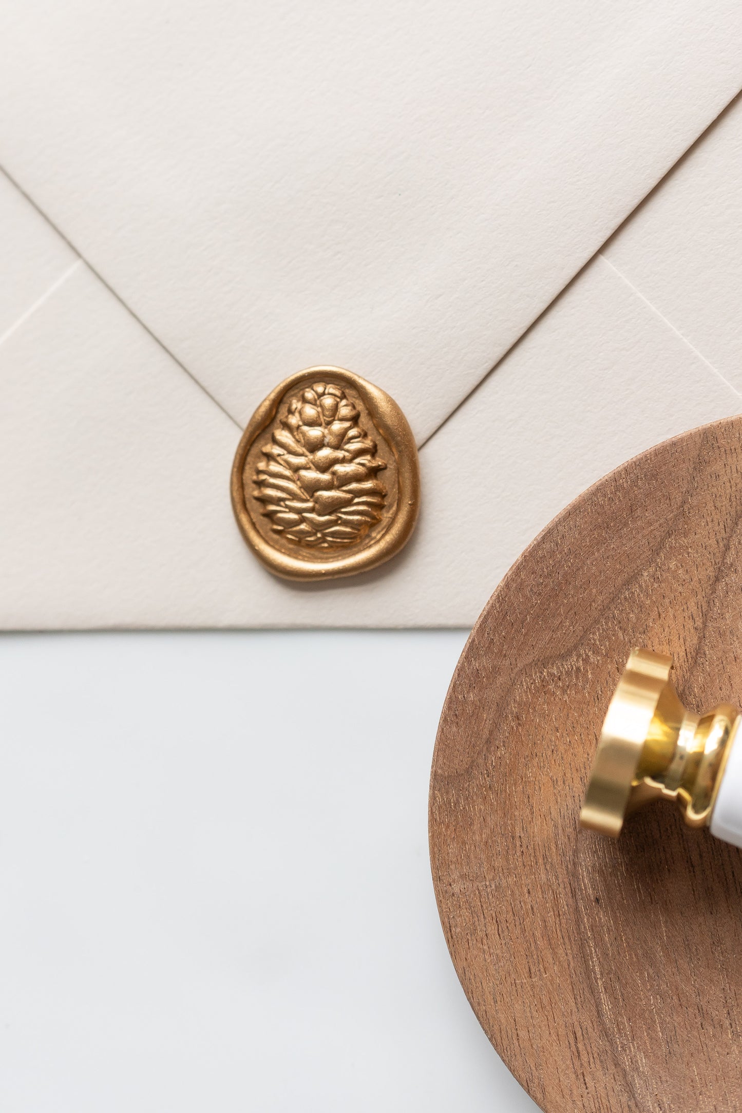 A pinecone wax seal stamp and beige envelope showcasing a gold pinecone wax seal, perfect for Holiday greeting cards
