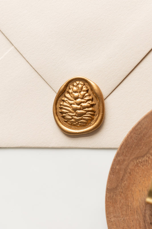 A beige envelope showcasing a gold pinecone wax seal, perfect for Holiday greeting cards

