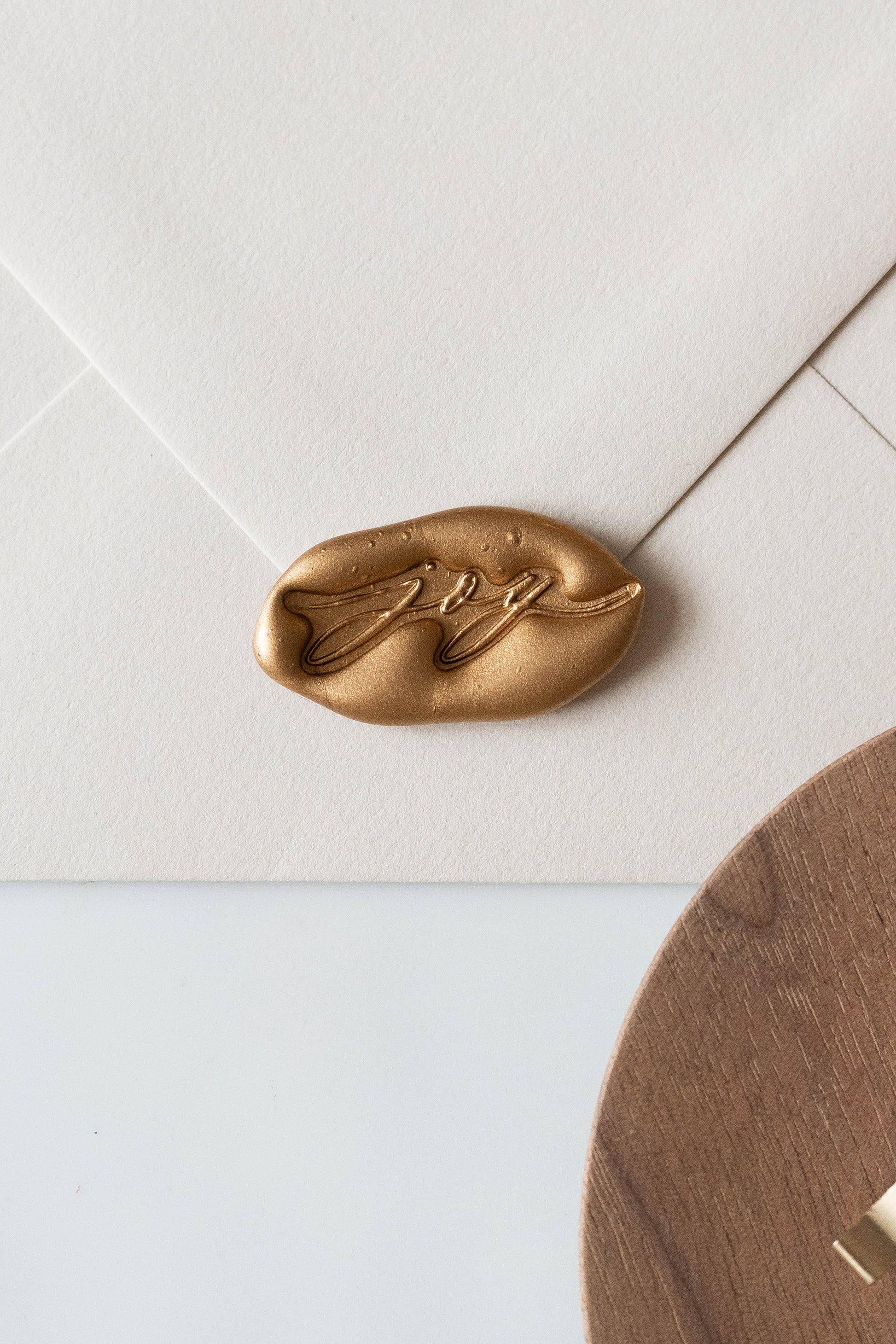 A beige envelope featuring a golden wax seal with the word joy spelled out, perfect for Holiday greeting cards