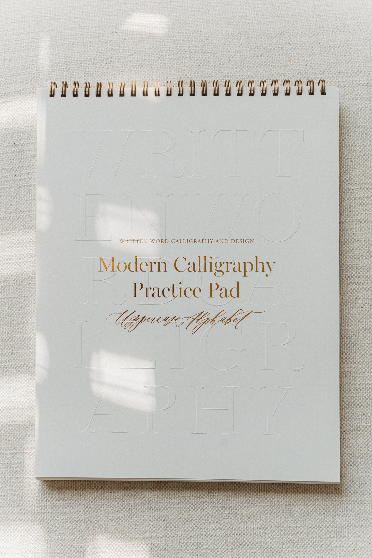 Modern calligraphy practice pad featuring an uppercase alphabet, with a gold spiral binding