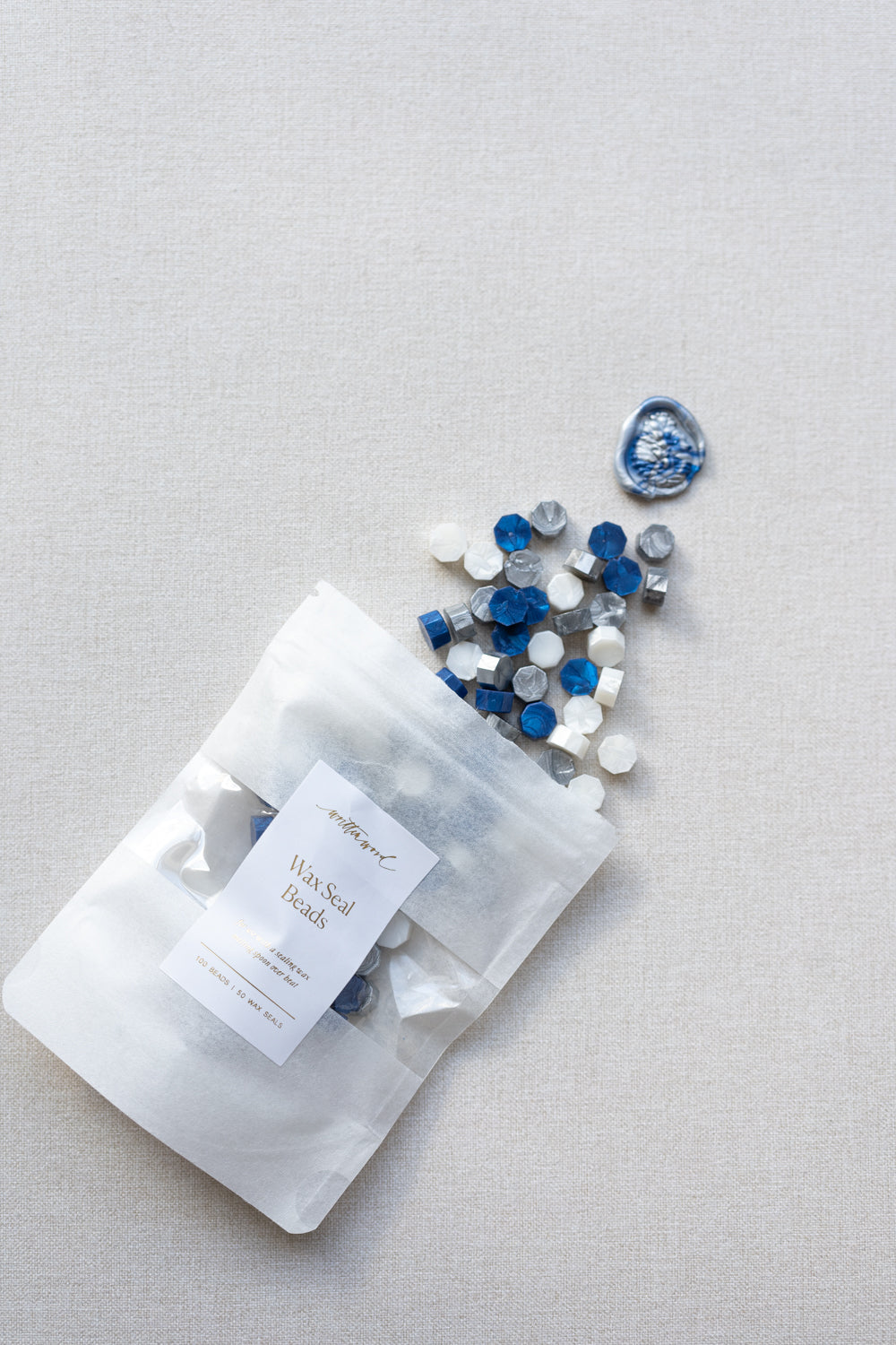 Starry night wax seal beads in blue, silver and white mix spilling from pouch on neutral linen background