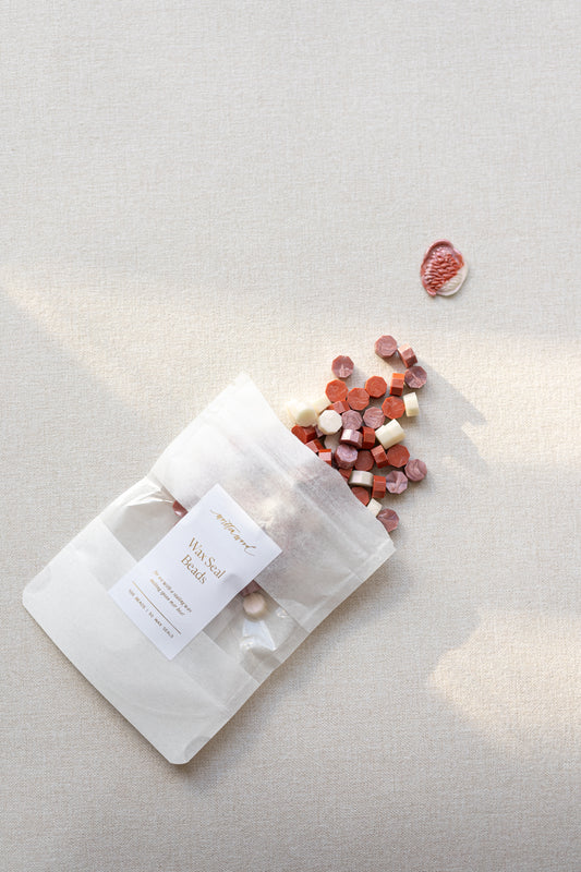 Wax seal beads in frosted blush color mix in labeled pouch with scattered beads and finished seal on linen surface