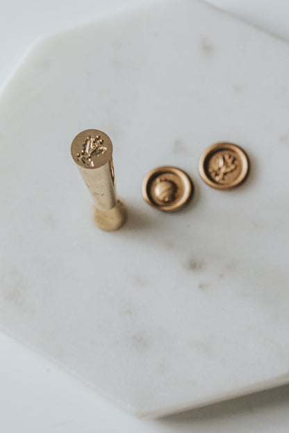Mini wax seal stamp with holly design, shown with matching gold wax seals on a white marble surface.