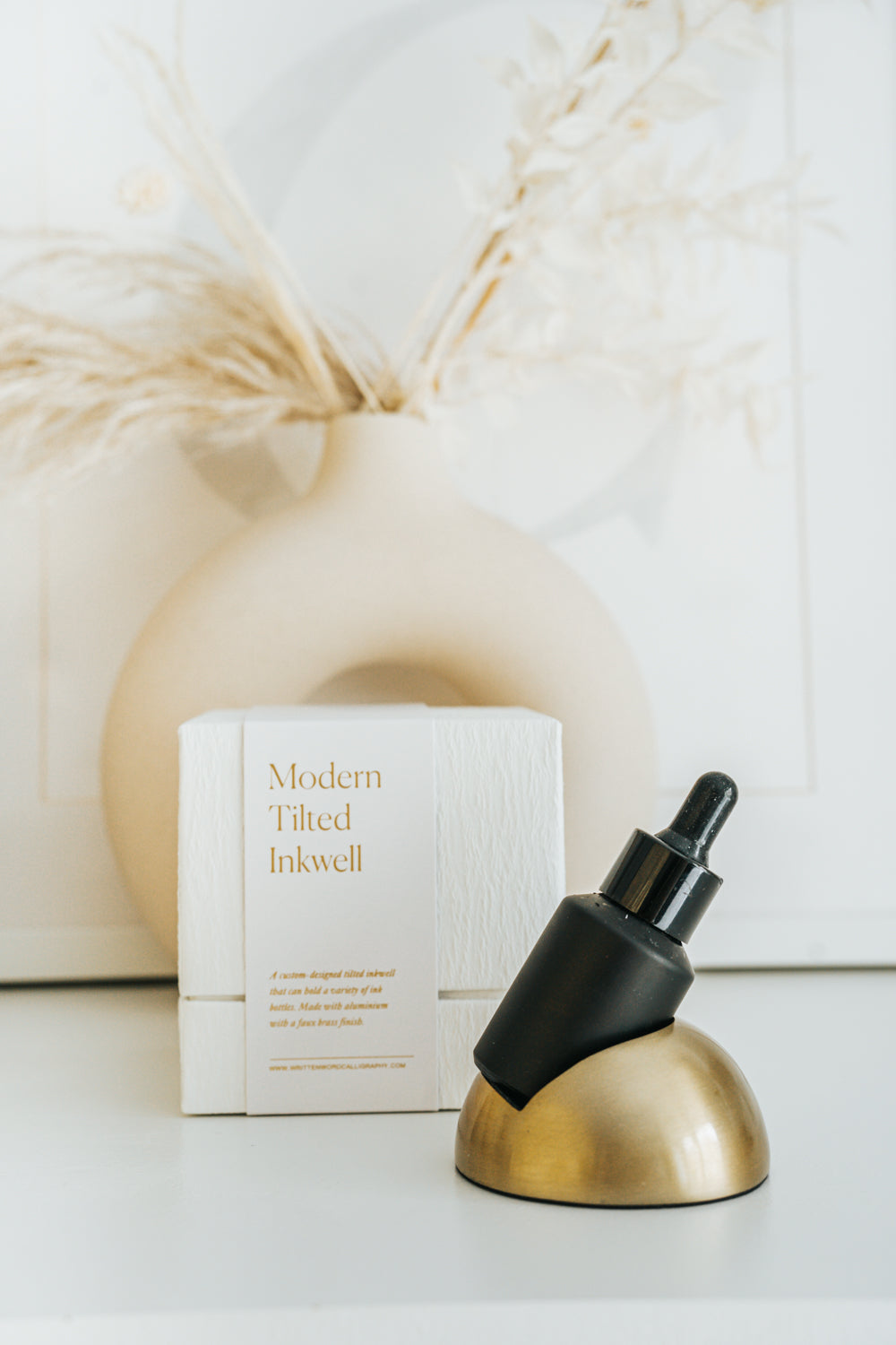Modern tilted inkwell with a faux brass finish, holding a black ink bottle. Stylish design for calligraphy or creative workspaces