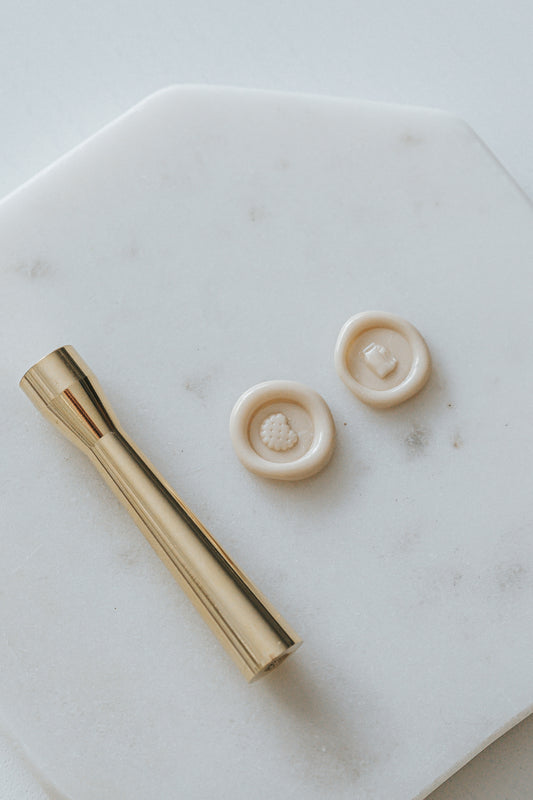 Gold miniature wax seal stamp with cookies and milk carton designs, placed on a white marble surface