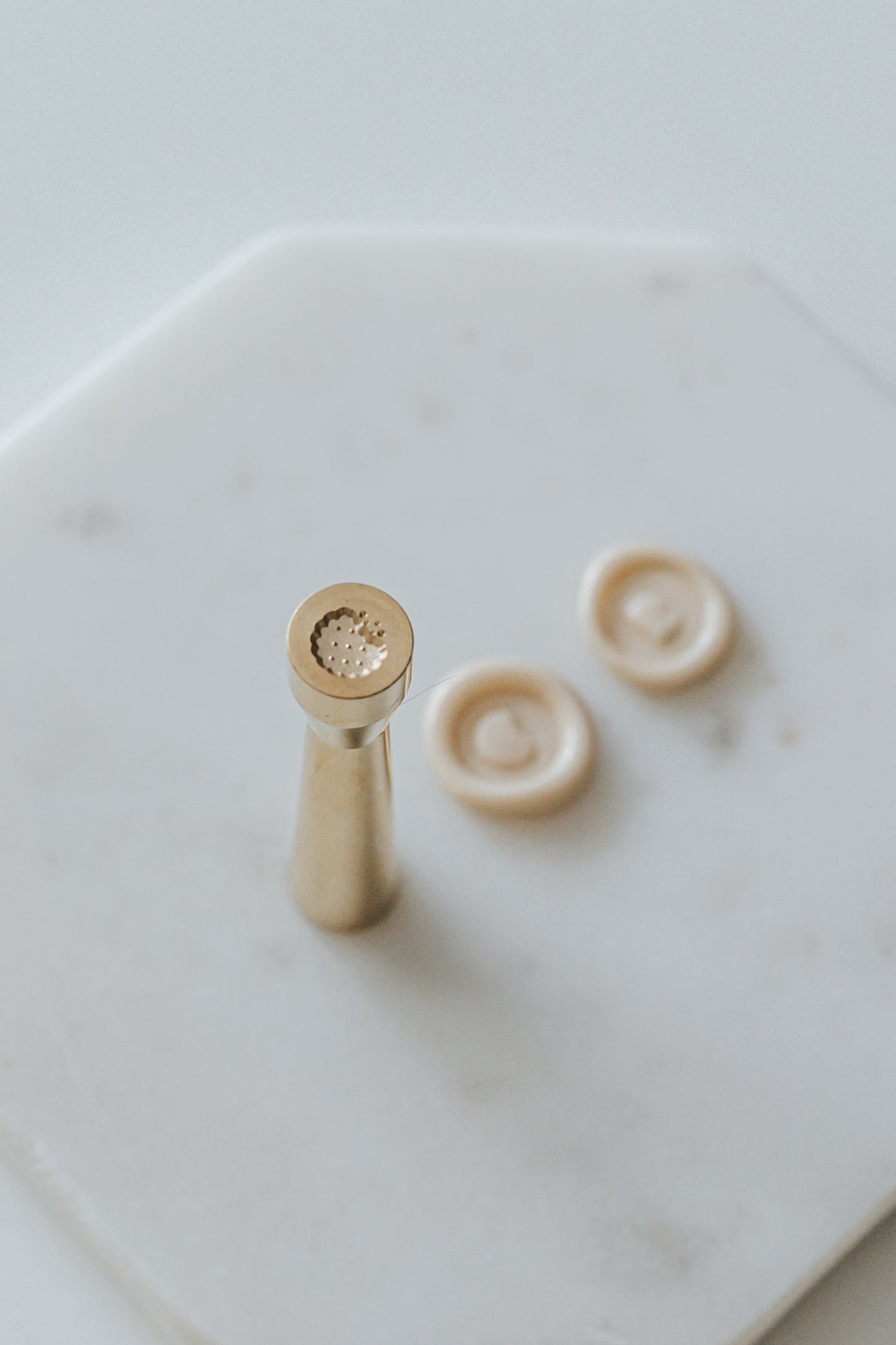 Mini wax seal stamp with a cookie design, displayed with matching beige wax seals on a white marble surface.