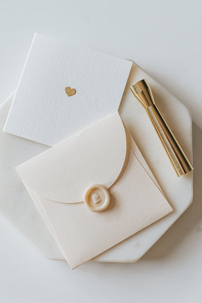 Elegant stationery with a gold heart detail and a sealed envelope, alongside a brass mini wax seal stamp on a marble plate