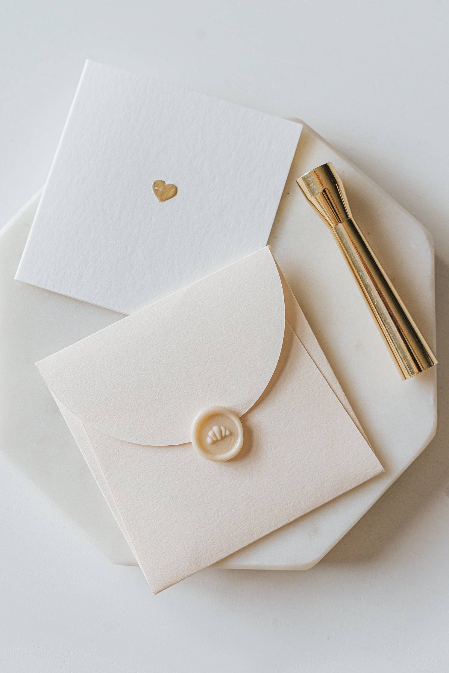 Elegant stationery with a gold heart detail and a sealed envelope, alongside a brass mini wax seal stamp on a marble plate