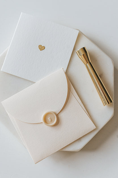 Elegant stationery with a gold heart detail and a sealed envelope, alongside a brass mini wax seal stamp on a marble plate