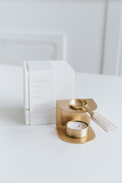 Elegant brass wax seal stove with a matching melting spoon and tealight candle, displayed beside its textured white packaging