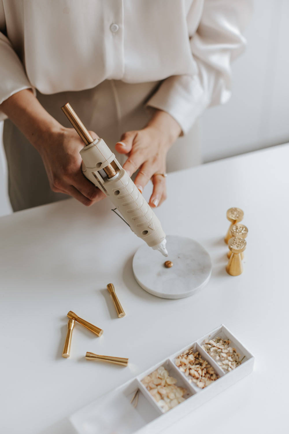 Applying sealing wax with a glue gun beside brass wax seal stamps and dried flowers to create custom wax seals for wedding invitations, cards, and gift wrapping.