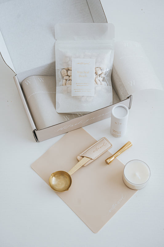 Mini wax seal starter kit with wax beads, brass spoon, seal stamp, candle, and mat, displayed with elegant packaging