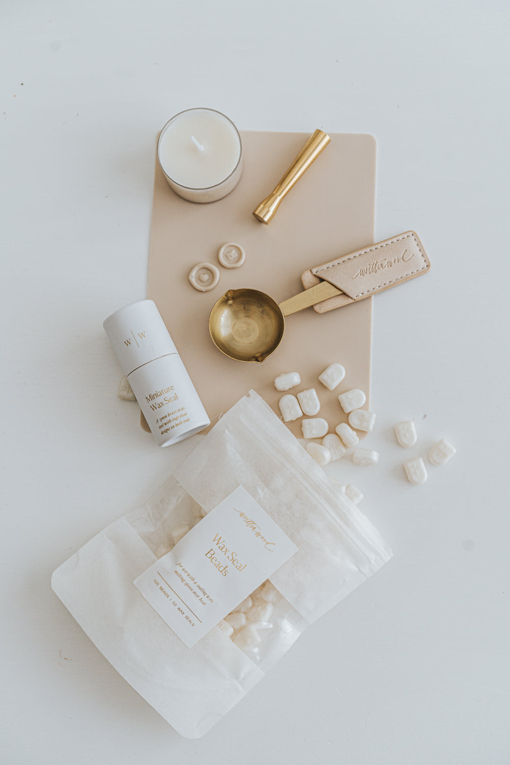 Mini wax seal starter kit with wax beads, brass spoon, seal stamp, candle, and mat, arranged neatly on a white surface