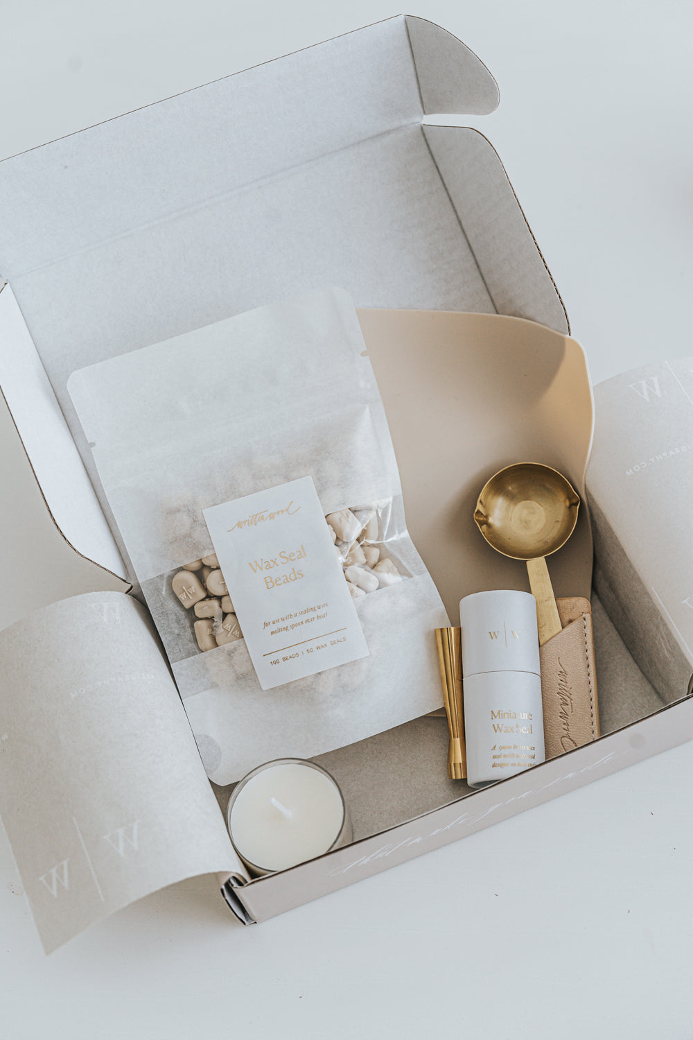 Mini wax seal starter kit in a box with wax beads, brass spoon, seal stamp, candle, and mat, neatly arranged