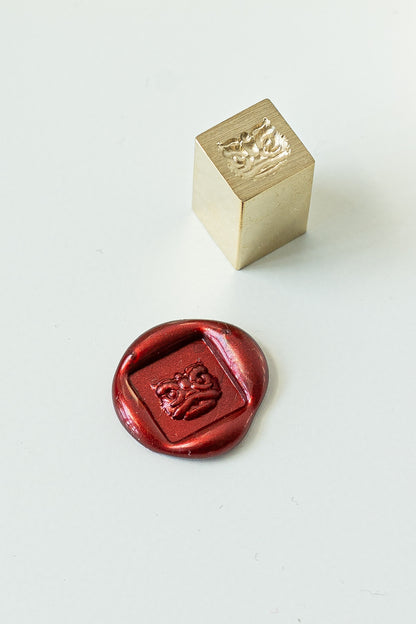 A square mini wax seal with a lion dance head engraved with a red wax seal showcasing the design