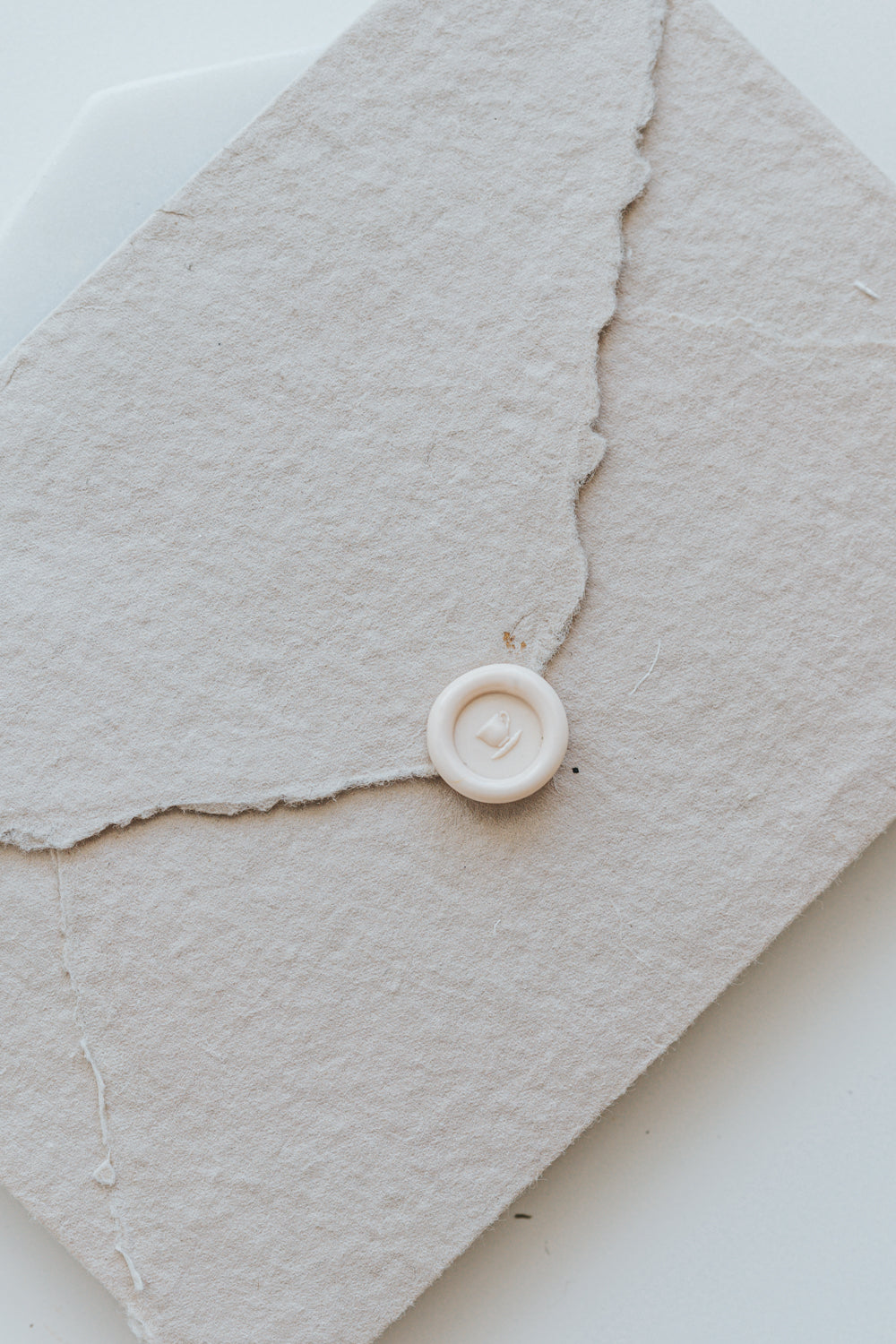 ​A mini 9mm blush wax seal with a 3D tea cup design on a textured taupe envelope