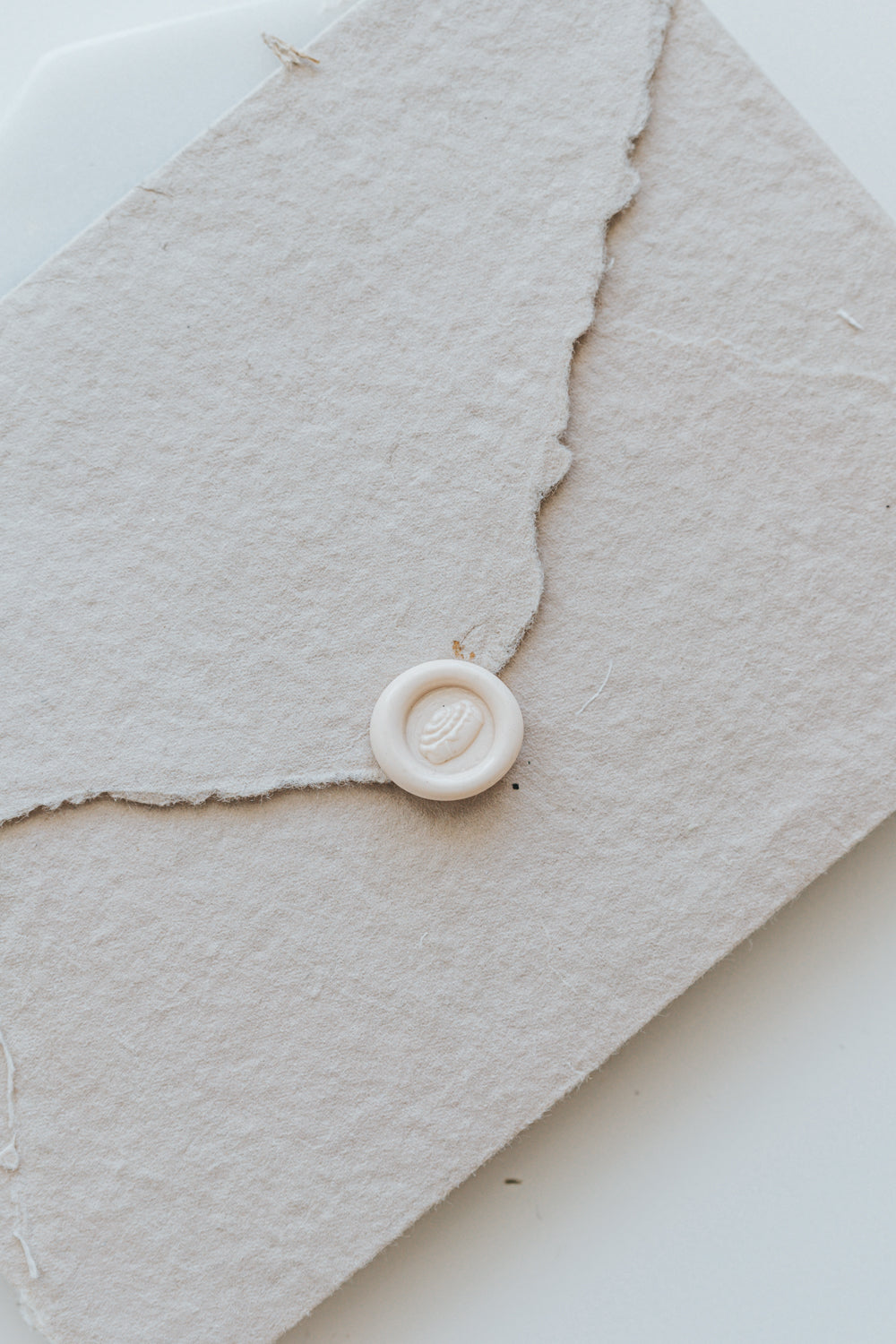​A mini 9mm blush wax seal with a 3D cinnamon bun design on a textured taupe envelope