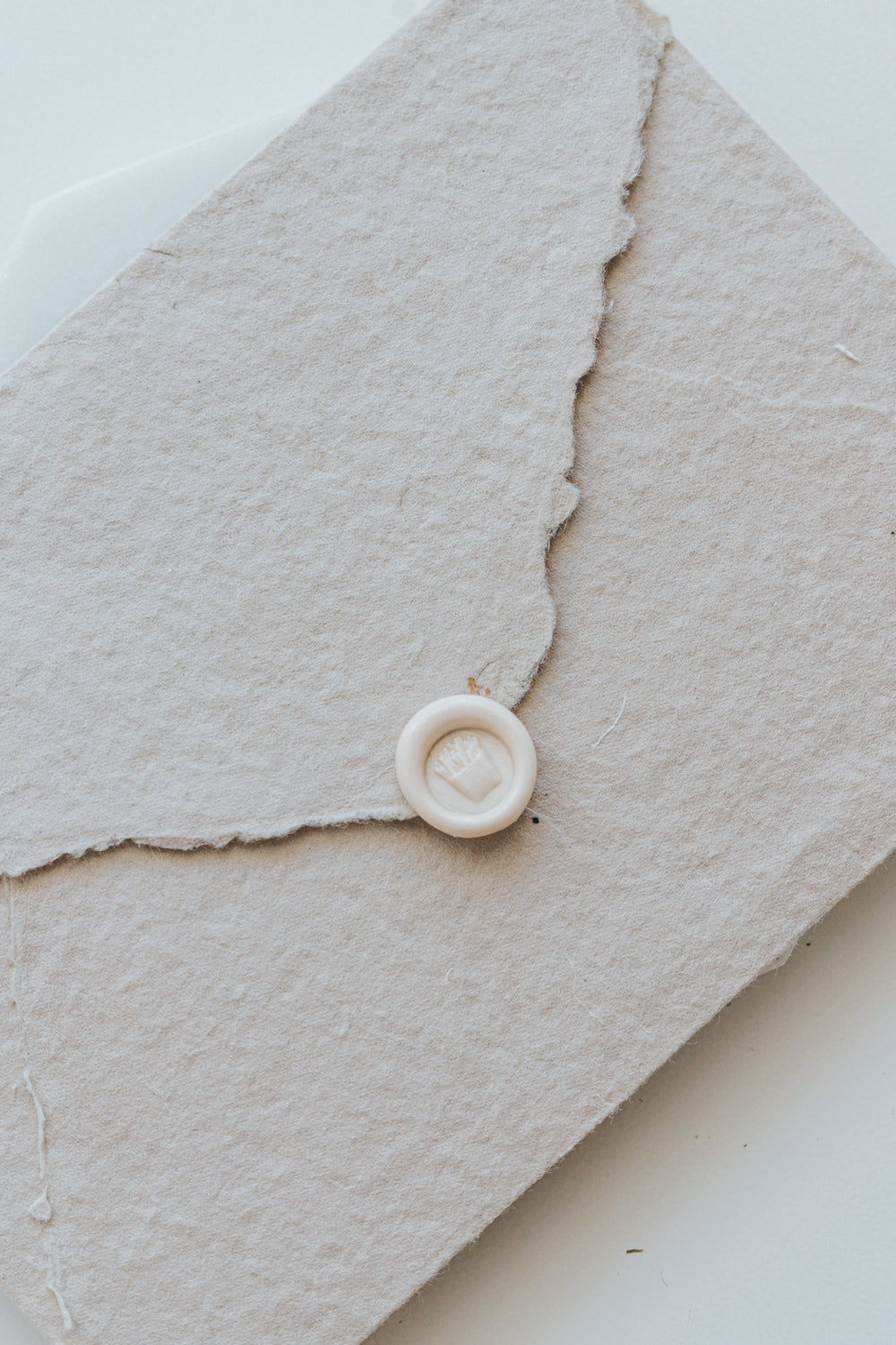 A mini 9mm blush wax seal with a 3D French fries design on a textured taupe envelope