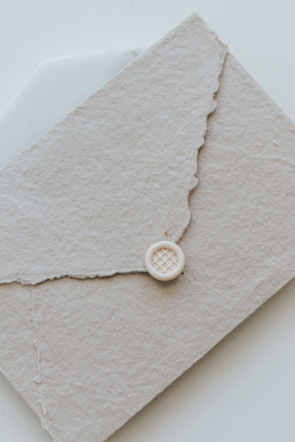 A mini 9mm blush wax seal with a 3D Belgian waffle design on a textured taupe envelope