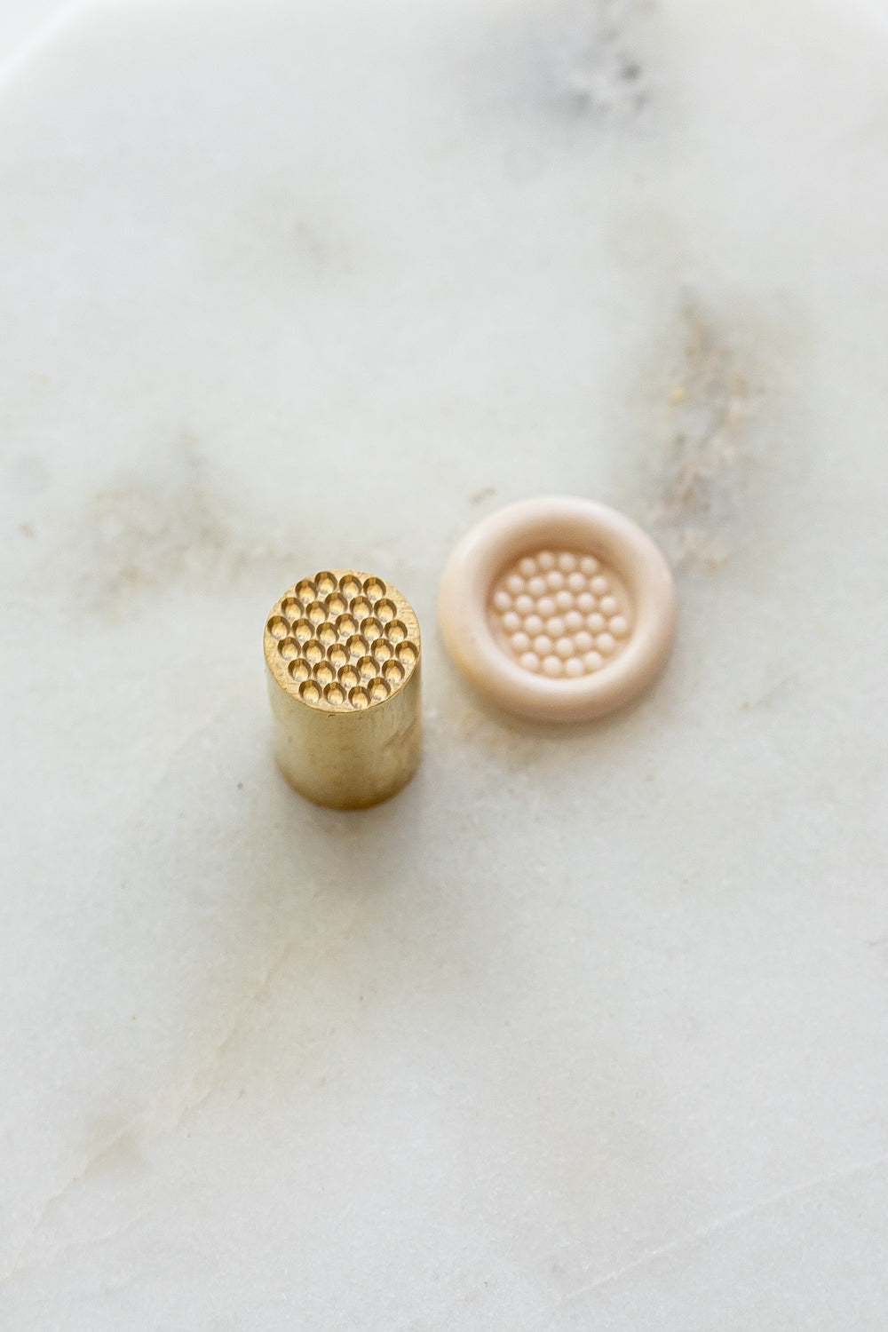 ​A mini brass wax seal stamp head with a 3D bubble waffle design beside a blush wax seal impression on a white marble surface