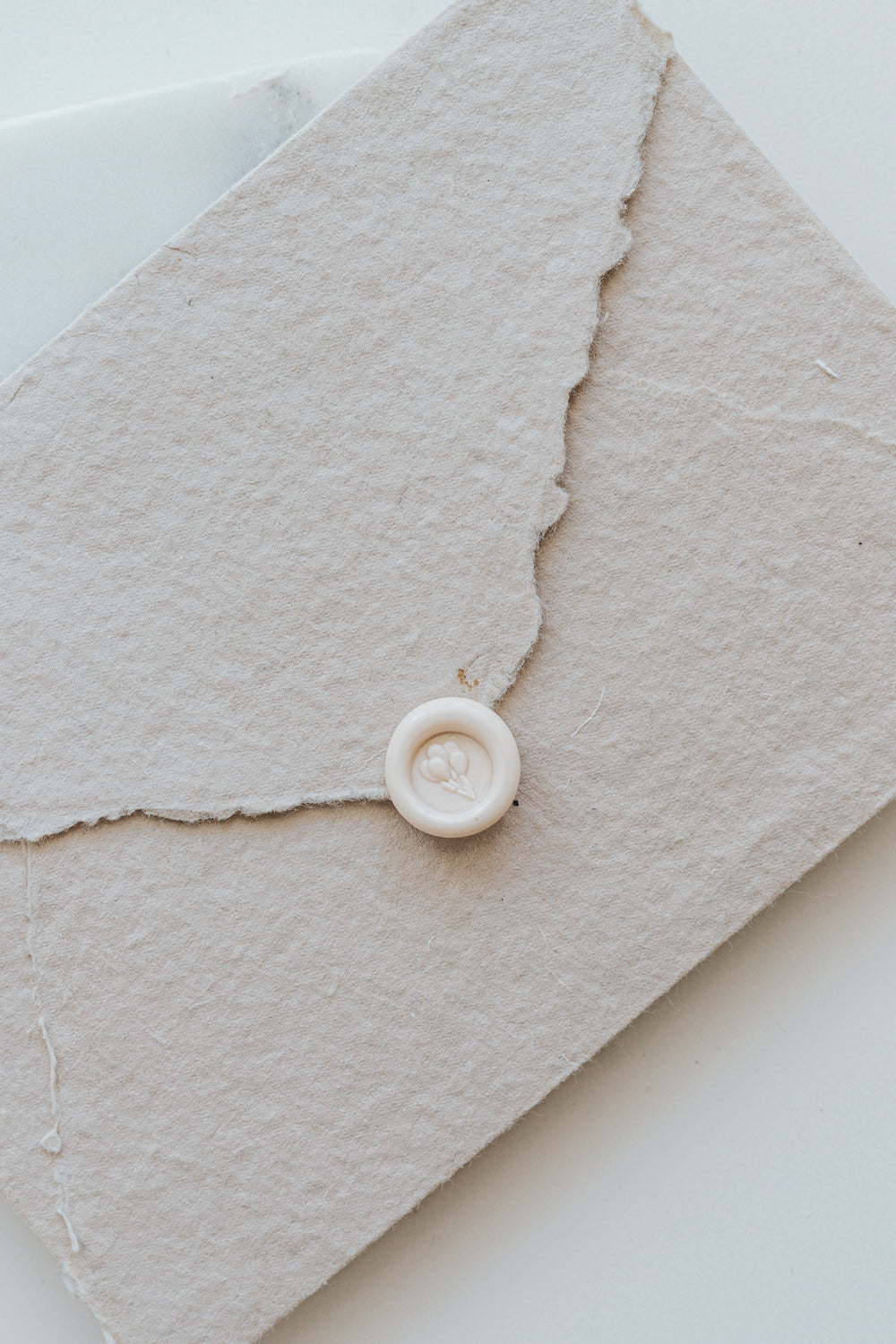 ​A mini 9mm blush wax seal with a 3D balloons design on a textured taupe envelope