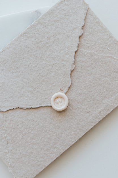​A mini 9mm blush wax seal with a 3D balloons design on a textured taupe envelope