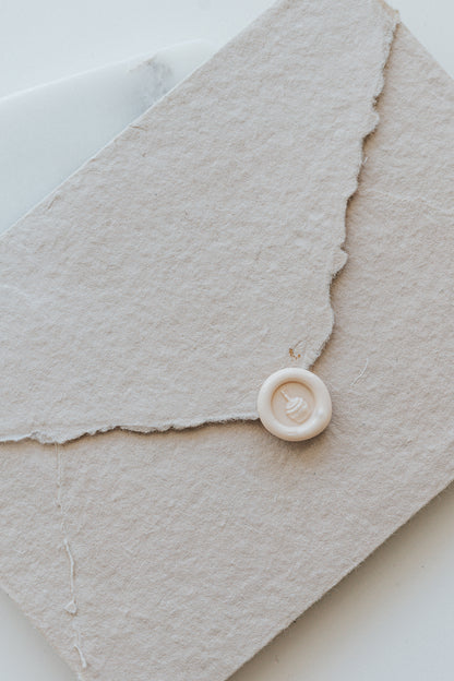 A mini 9mm blush wax seal with a 3D French fries design on a textured taupe envelope