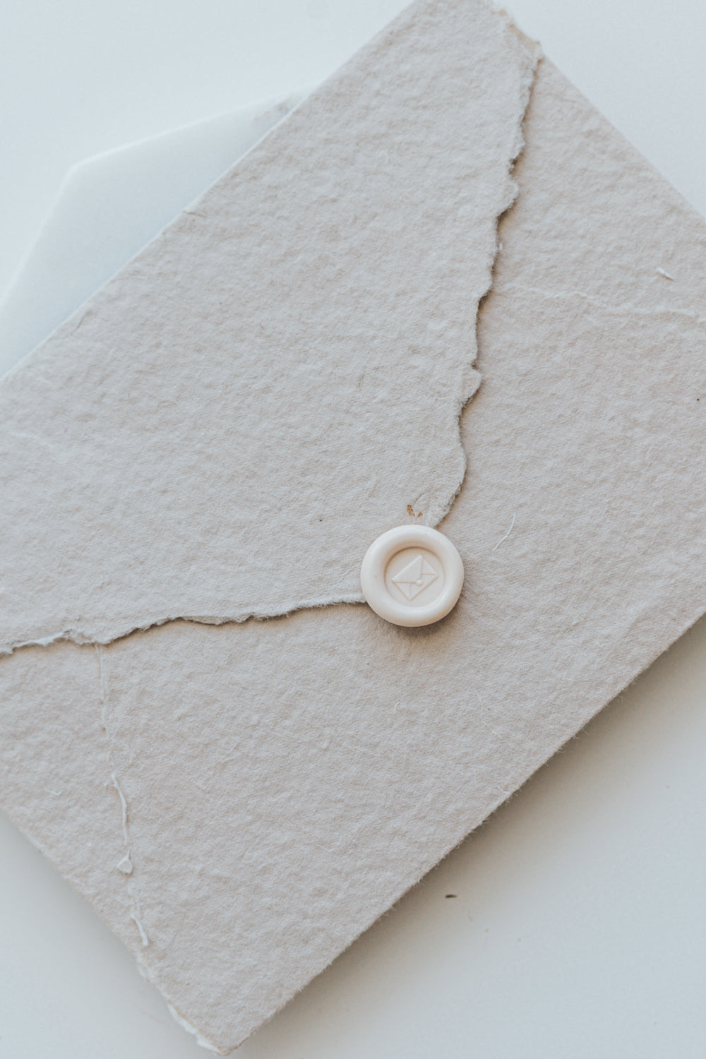 ​A mini 9mm blush wax seal with an envelope design on a textured taupe envelope