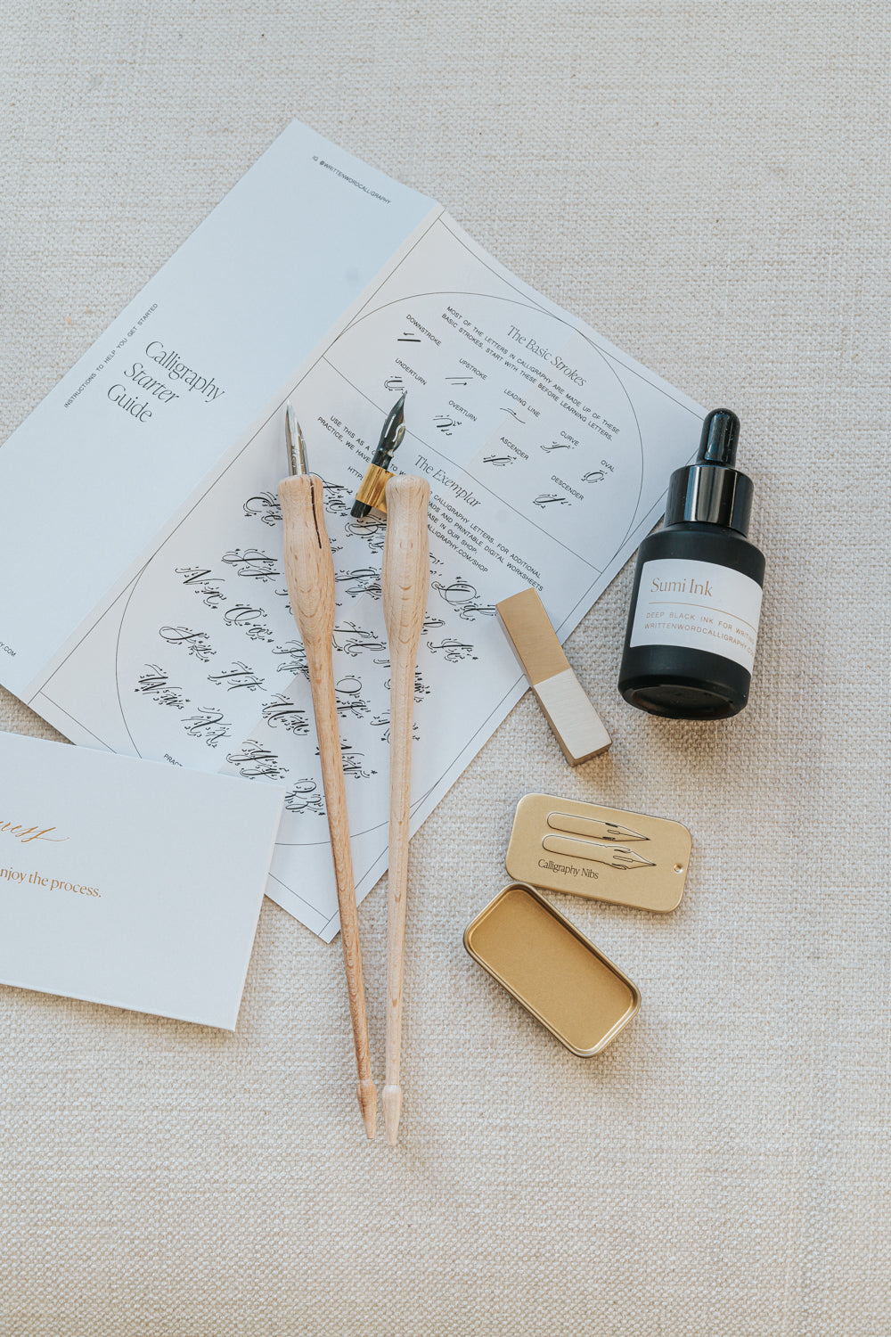 Mini Calligraphy Starter Kit with dual-purpose pens, sumi ink, brass pen rest, nibs, and guide, displayed on a textured surface