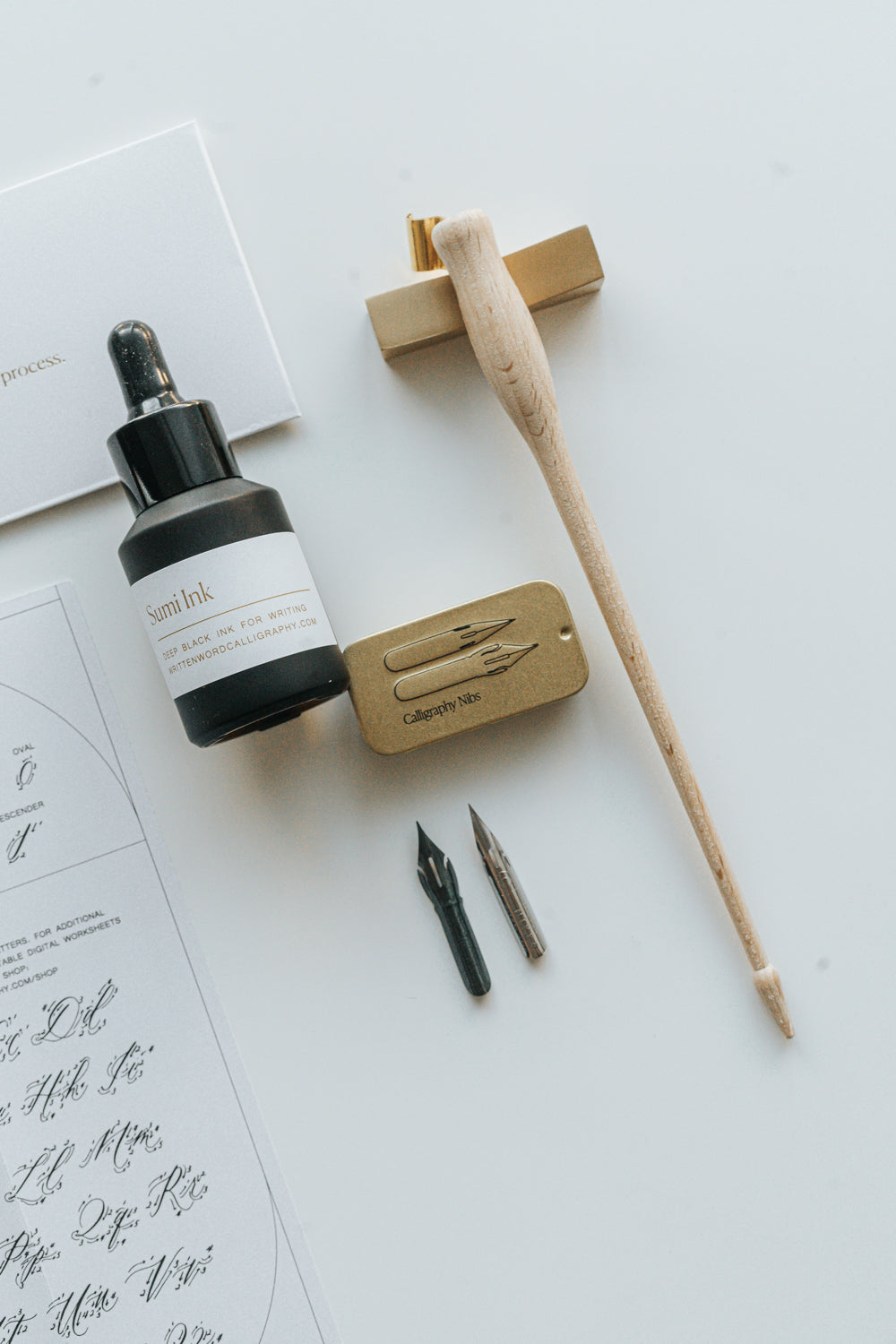 Calligraphy set with sumi ink, a wooden oblique pen holder, nibs, and a metal nib tin, displayed on a white surface