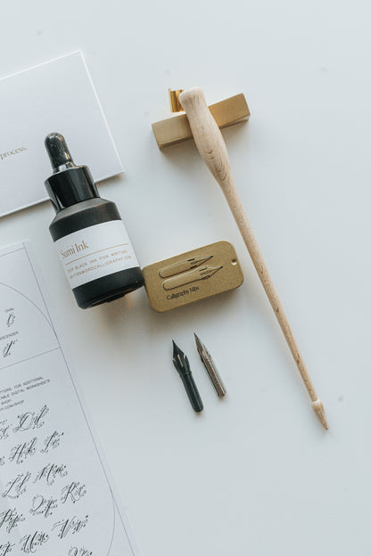 Calligraphy set with sumi ink, a wooden oblique pen holder, nibs, and a metal nib tin, displayed on a white surface