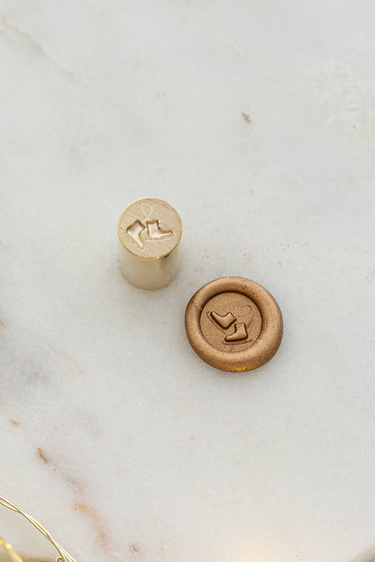 Close-up of festive wax seal stamp featuring a pair of ice skates in gold wax, from Written Word Calligraphy’s Holiday Collection.