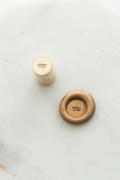 Close-up of mini wax seal stamp with “TO” design in gold wax, part of Written Word Calligraphy’s Holiday Collection.