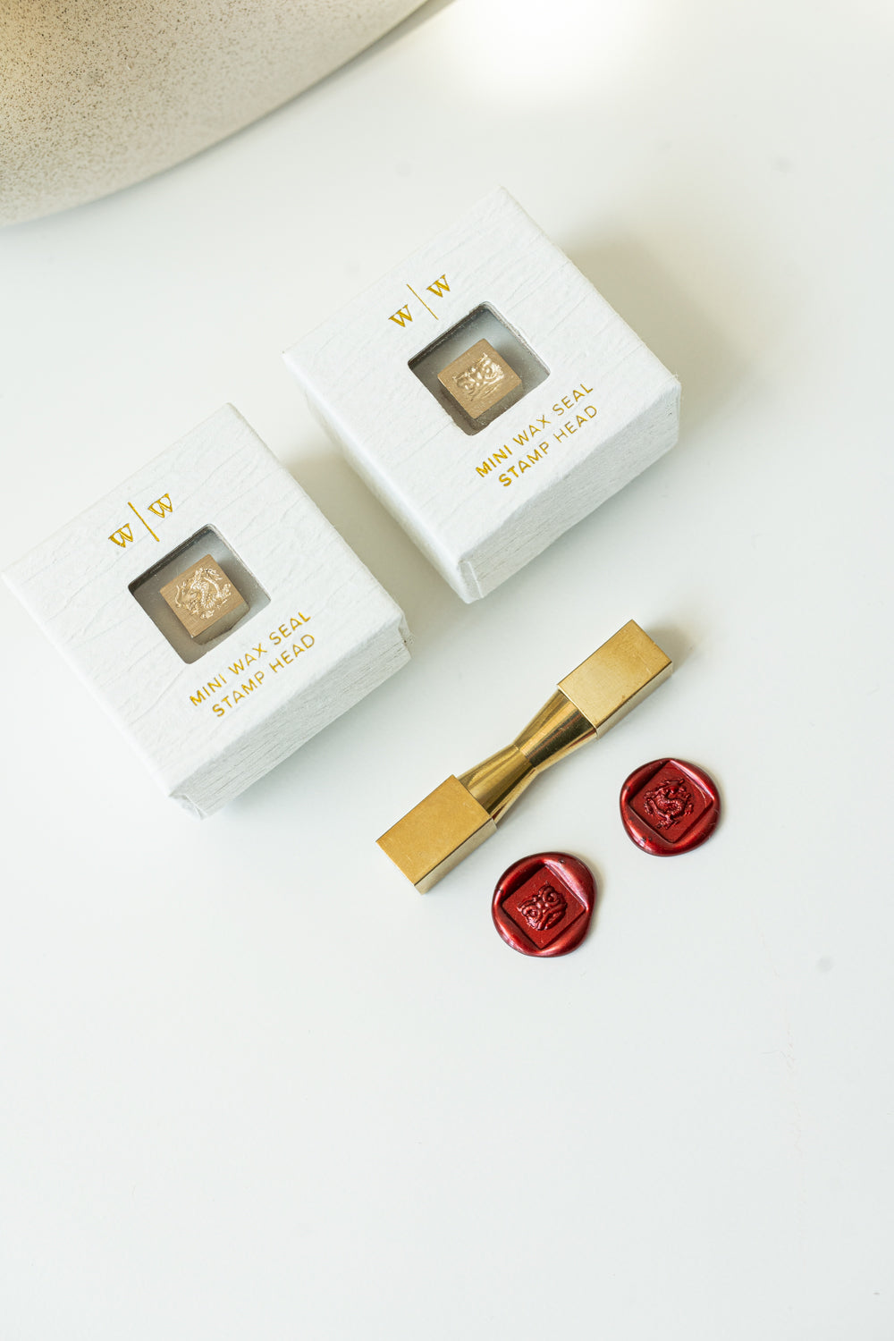 Two square mini wax seals with a dragon and lion dance head design packaged in a white ring-style box, next to a wax seal stamp and two red wax seals