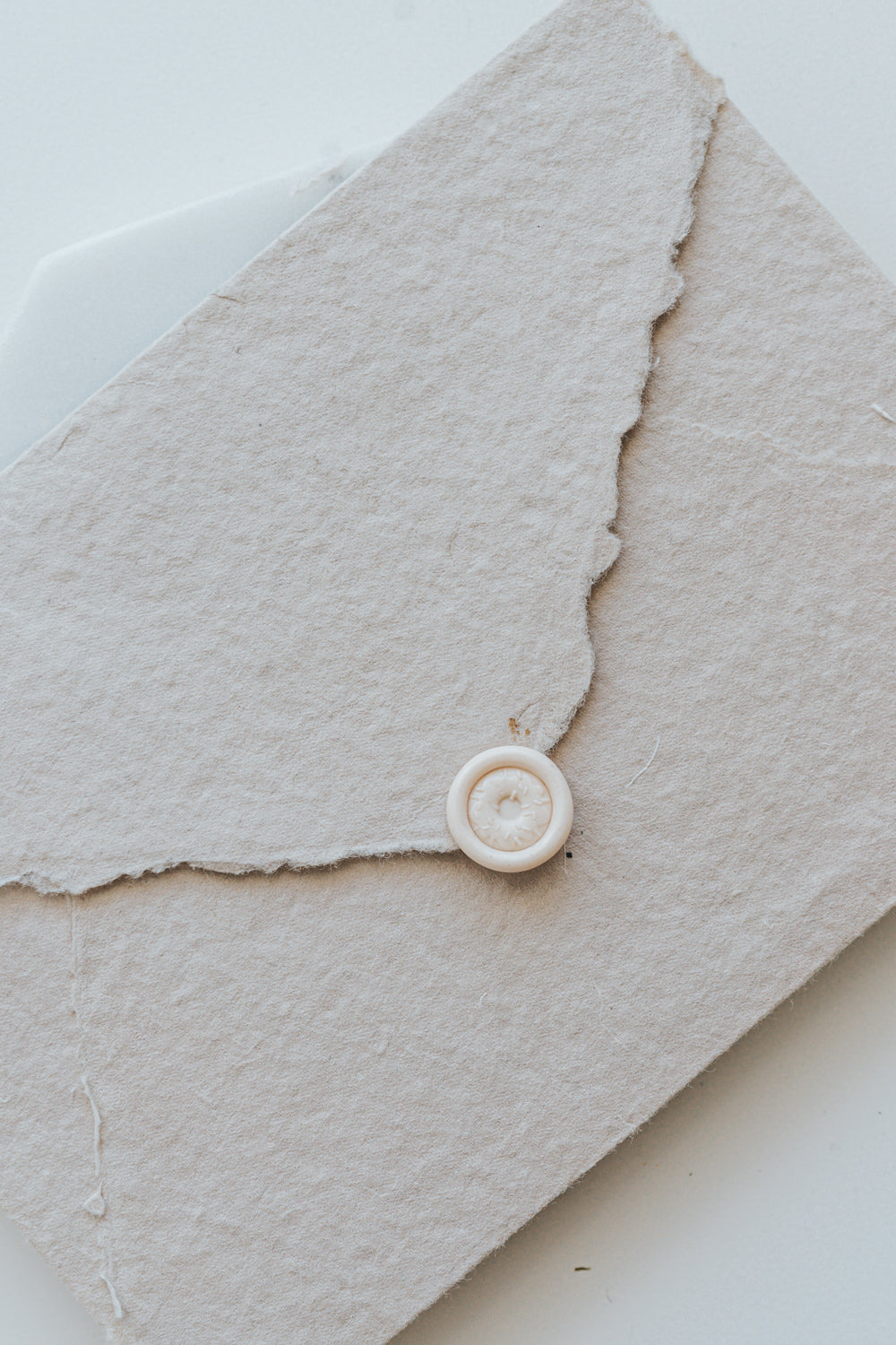 A mini 9mm blush wax seal with a 3D donut design on a textured taupe envelope